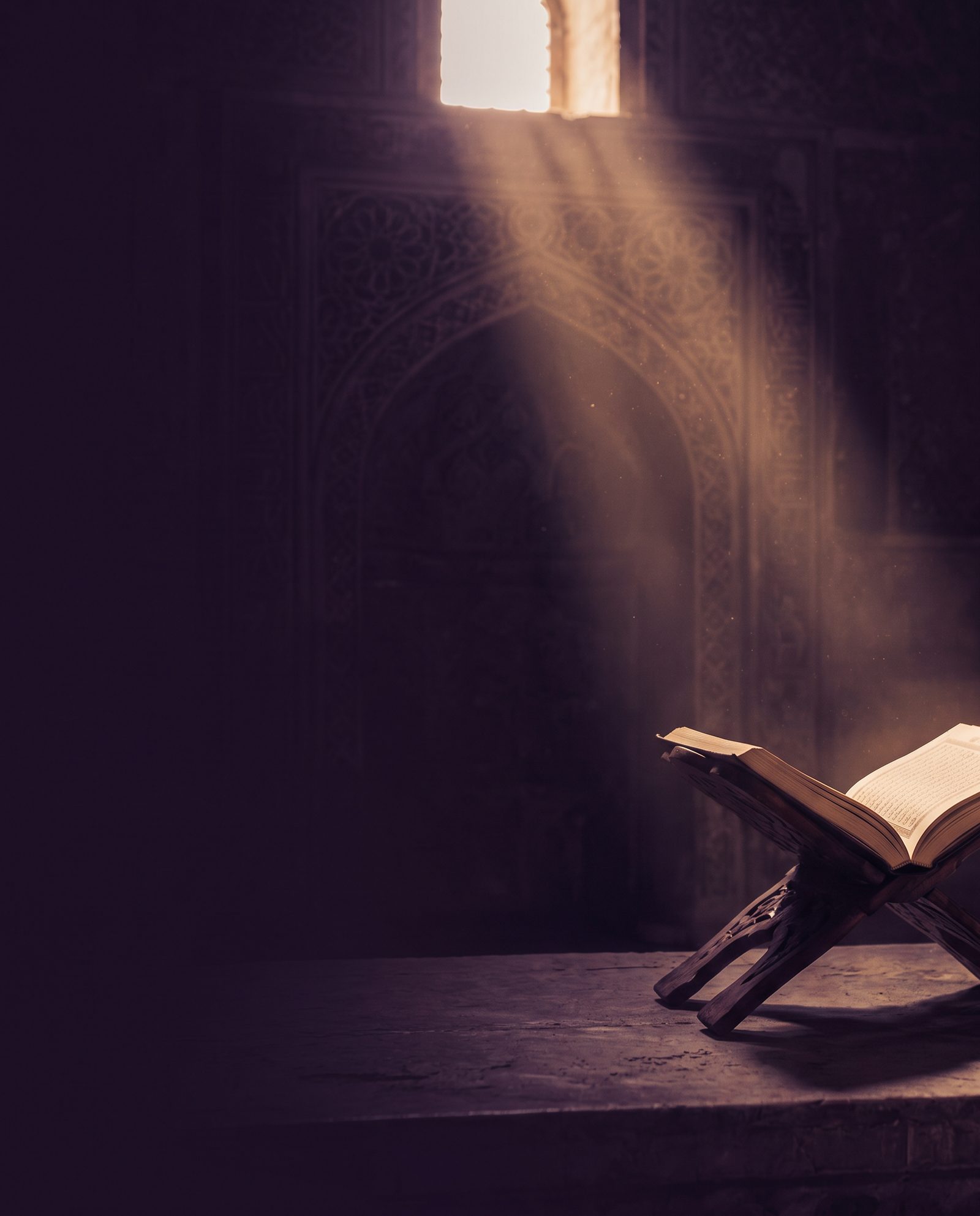 A mushaf resting on a wooden stand with a beam of warm light through Islamic architecture.